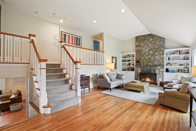 living room featuring wood finished floors, lofted ceiling, built in shelves, a stone fireplace, and stairs