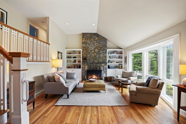 living area with plenty of natural light, light wood-style floors, lofted ceiling, a stone fireplace, and built in features