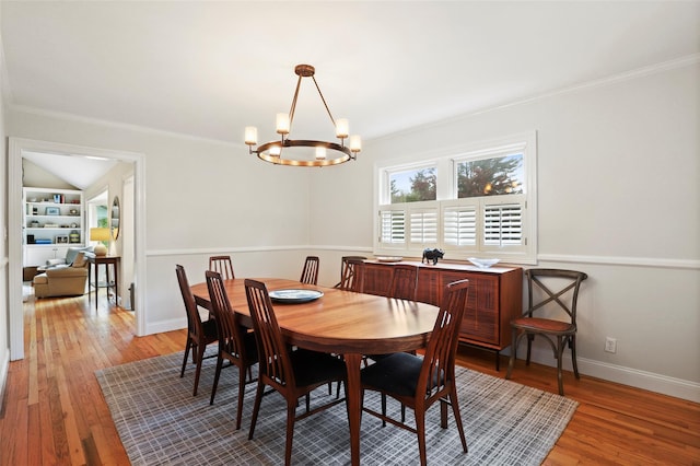 dining space featuring a chandelier, ornamental molding, light wood-style flooring, baseboards, and built in shelves