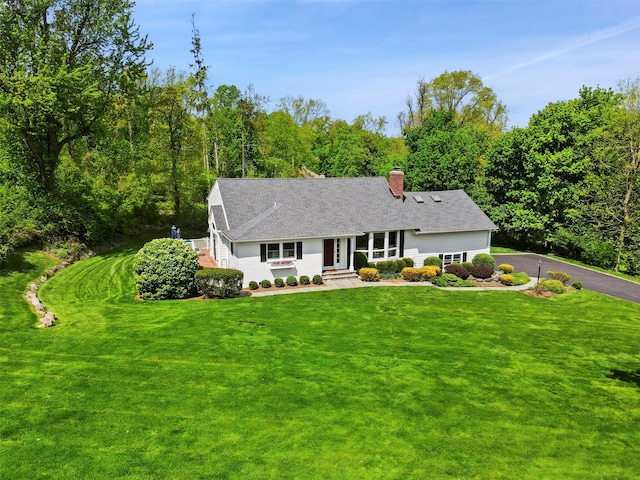view of front of house featuring a chimney, a front lawn, driveway, and a shingled roof