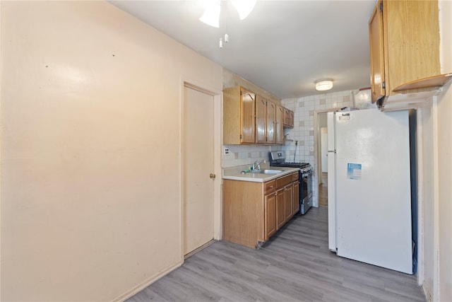 kitchen featuring freestanding refrigerator, decorative backsplash, light wood-style floors, light countertops, and stainless steel range with gas stovetop