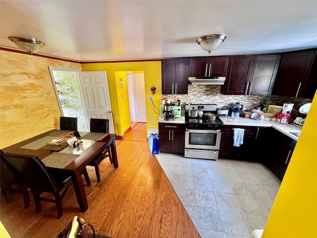 kitchen featuring dark brown cabinetry, stainless steel range with gas cooktop, light countertops, under cabinet range hood, and backsplash