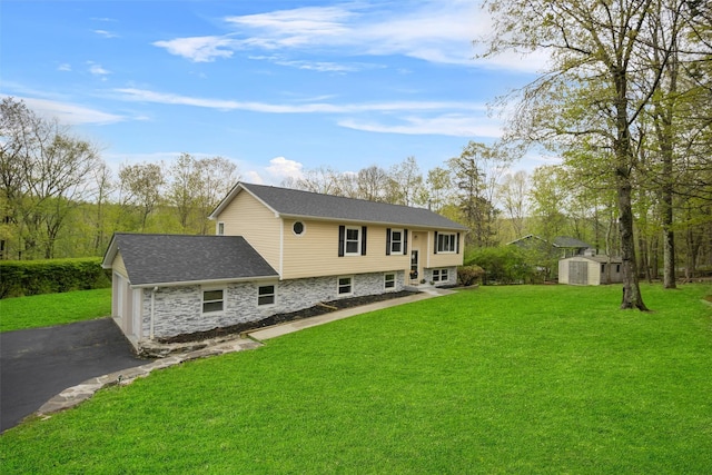 back of property featuring an outbuilding, aphalt driveway, a yard, a storage unit, and stone siding