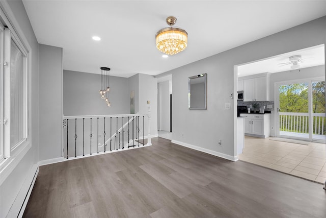spare room with wood finished floors, baseboards, baseboard heating, recessed lighting, and ceiling fan with notable chandelier