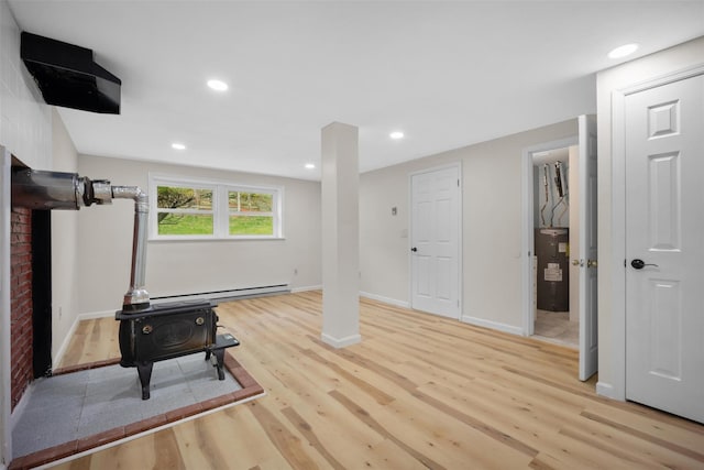 workout area with a wood stove, light wood-style flooring, baseboard heating, and electric water heater