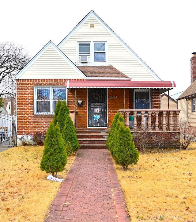 view of front of home with brick siding, a front lawn, covered porch, and cooling unit