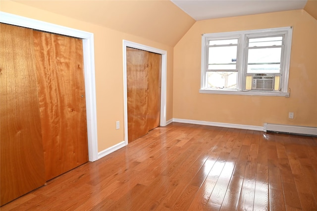 unfurnished bedroom with two closets, baseboards, lofted ceiling, a baseboard radiator, and hardwood / wood-style flooring