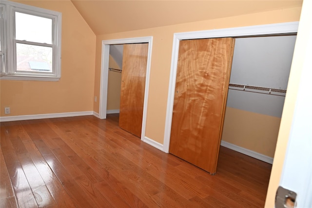 unfurnished bedroom with baseboards, vaulted ceiling, two closets, and wood finished floors