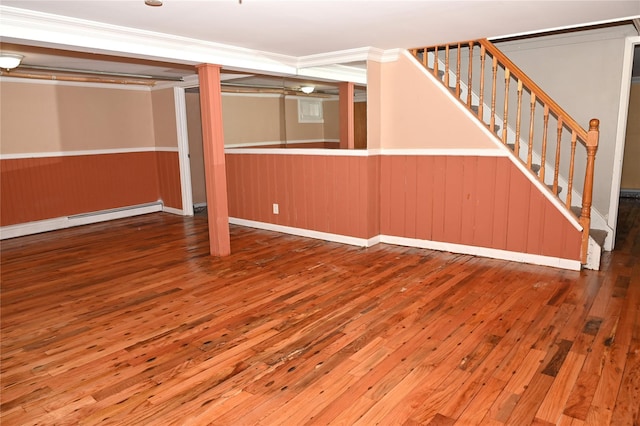 finished basement with crown molding, wainscoting, stairway, a baseboard radiator, and wood-type flooring