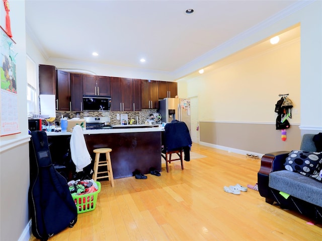 kitchen featuring appliances with stainless steel finishes, light wood-style floors, a breakfast bar area, tasteful backsplash, and ornamental molding