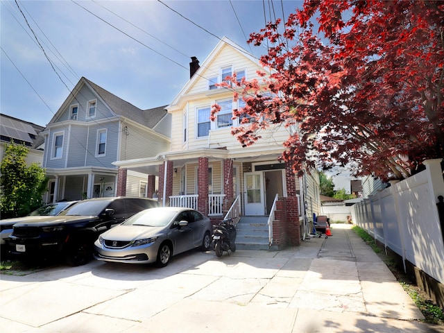 view of front facade with a porch, a carport, brick siding, fence, and concrete driveway