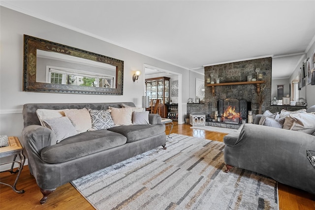 living area featuring ornamental molding, wood finished floors, and a stone fireplace