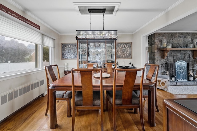 dining room featuring radiator, wood finished floors, crown molding, and a fireplace