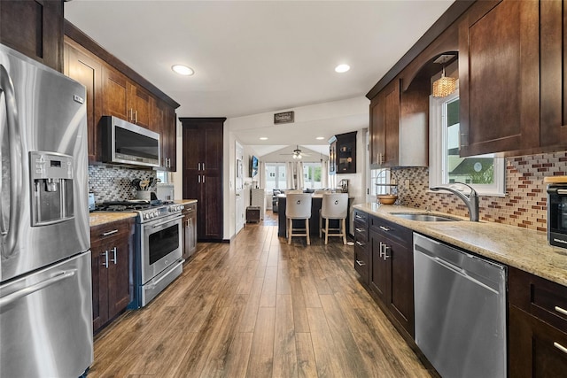kitchen featuring appliances with stainless steel finishes, a sink, dark wood-style flooring, dark brown cabinetry, and light stone countertops