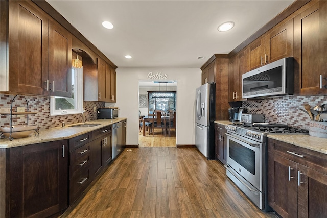 kitchen with appliances with stainless steel finishes, a sink, dark wood-type flooring, tasteful backsplash, and recessed lighting