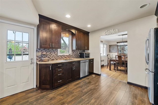 kitchen with stainless steel appliances, a sink, dark brown cabinetry, dark wood-style flooring, and baseboards