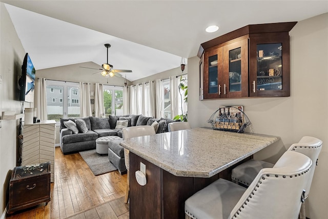 kitchen featuring hardwood / wood-style floors, a peninsula, ceiling fan, a breakfast bar, and lofted ceiling