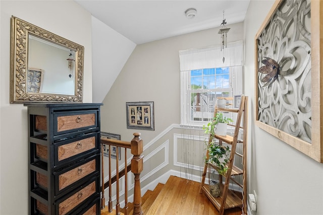 stairs with wood finished floors, a decorative wall, and a wainscoted wall