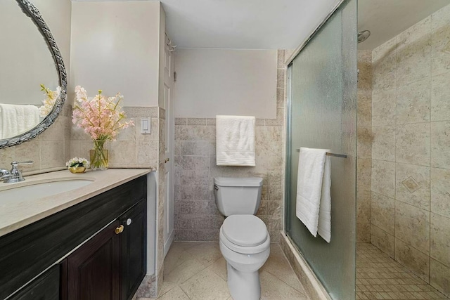 bathroom featuring tile walls, a shower stall, toilet, tile patterned floors, and vanity