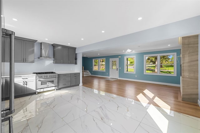 kitchen with wall chimney range hood, high end stainless steel range, open floor plan, gray cabinetry, and baseboards