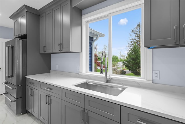 kitchen with gray cabinetry, high quality fridge, light stone counters, and a sink