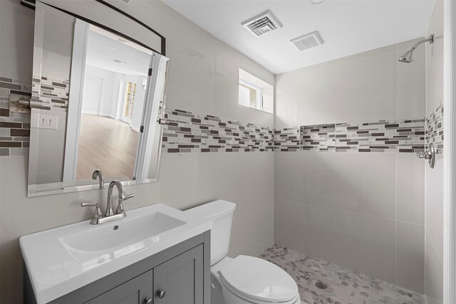 bathroom with toilet, tile walls, vanity, visible vents, and tiled shower