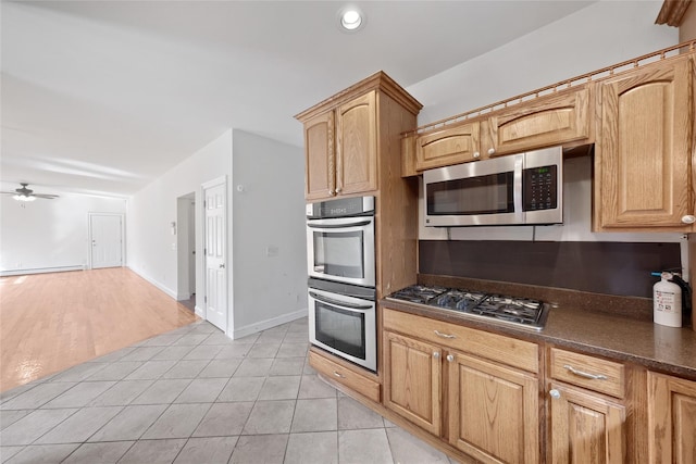 kitchen with light tile patterned flooring, dark countertops, ceiling fan, stainless steel appliances, and a baseboard heating unit