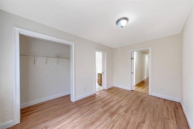 unfurnished bedroom featuring baseboards, a closet, light wood-type flooring, and ensuite bath