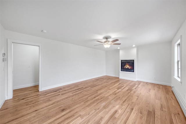 unfurnished living room with a ceiling fan, light wood-type flooring, baseboards, a baseboard heating unit, and a glass covered fireplace