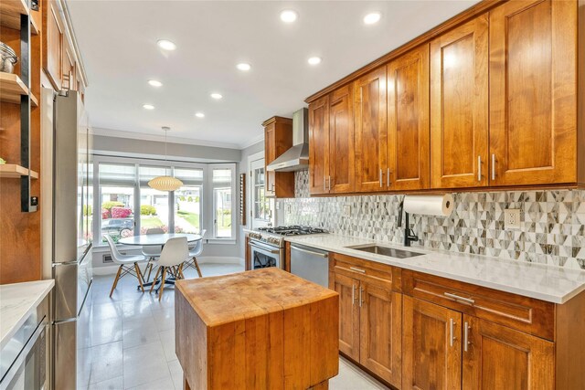 kitchen featuring wall chimney exhaust hood, ornamental molding, a sink, recessed lighting, and brown cabinetry