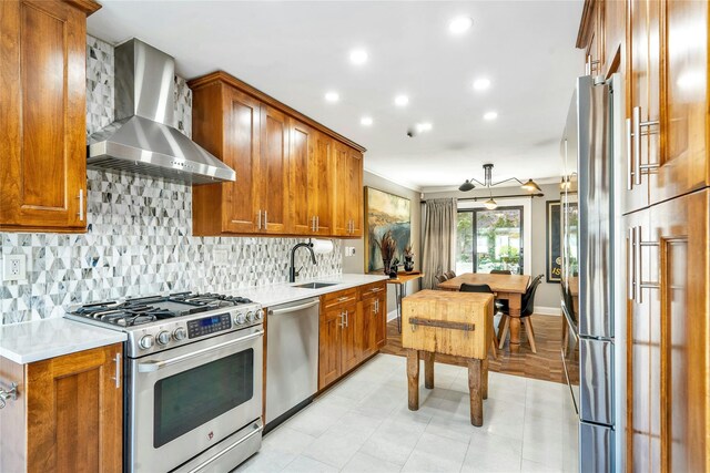 kitchen with stainless steel appliances, wall chimney exhaust hood, a sink, brown cabinetry, and recessed lighting