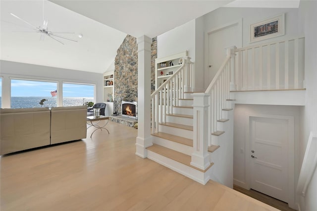 stairs with a fireplace, a water view, high vaulted ceiling, and wood finished floors