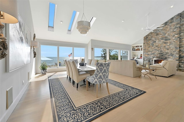 dining space featuring a water view, ceiling fan with notable chandelier, high vaulted ceiling, and wood finished floors