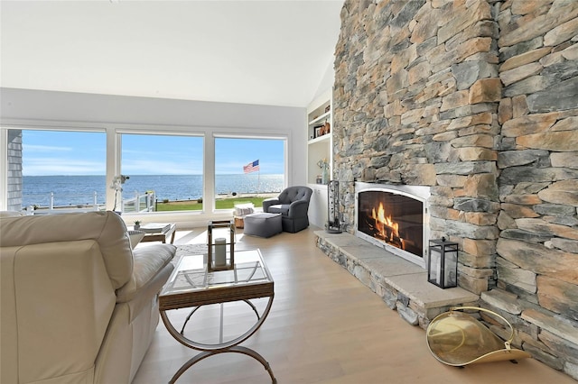 living area featuring vaulted ceiling, a stone fireplace, built in shelves, a water view, and wood finished floors