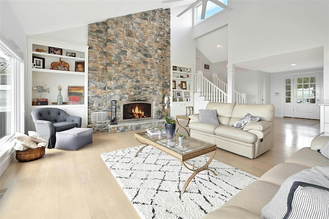living room featuring built in features, a stone fireplace, high vaulted ceiling, and wood finished floors