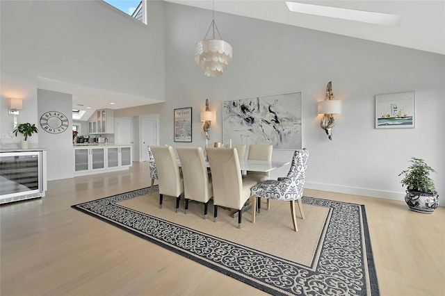 dining room featuring a skylight, wood finished floors, wine cooler, an inviting chandelier, and baseboards