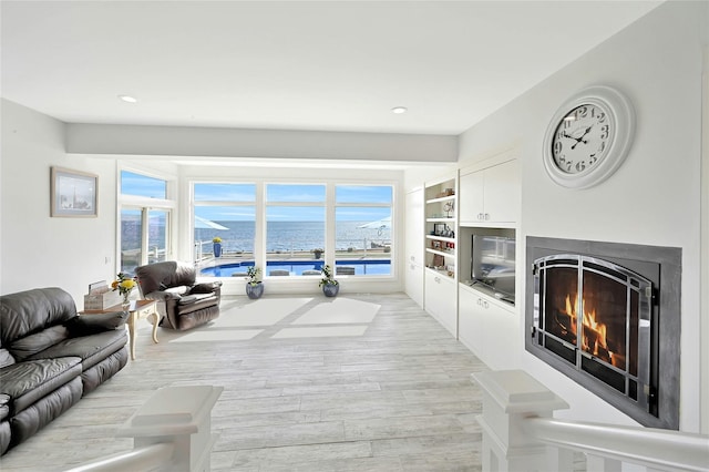 living room featuring a warm lit fireplace, light wood-style flooring, and recessed lighting