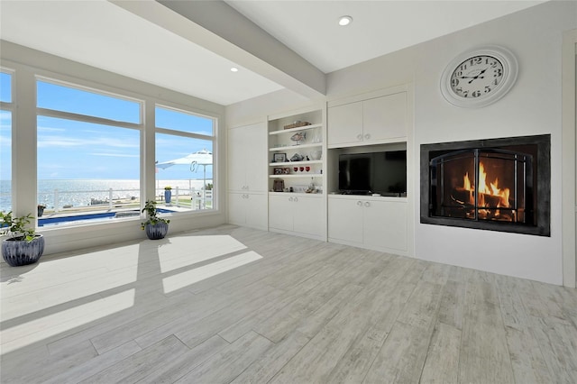 unfurnished living room featuring a water view, wood finished floors, a lit fireplace, beamed ceiling, and recessed lighting
