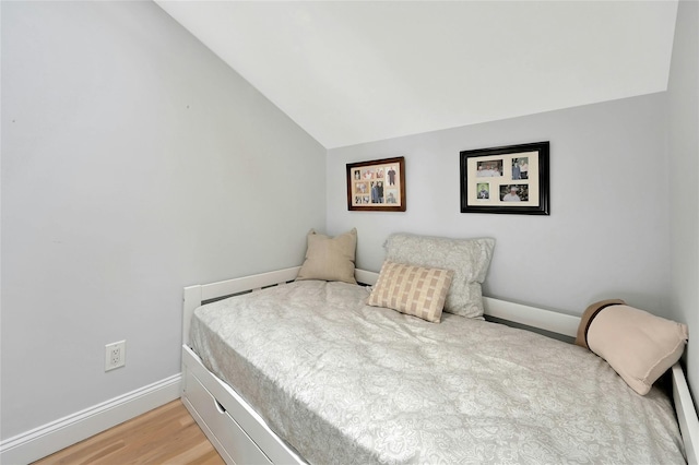bedroom with baseboards, light wood-type flooring, and vaulted ceiling
