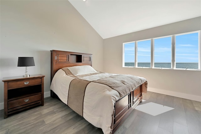 bedroom with a water view, vaulted ceiling, wood finished floors, and baseboards