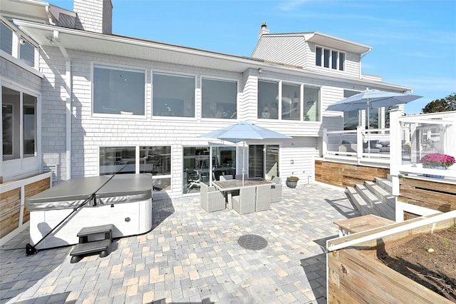 back of property featuring a chimney, outdoor dining space, a patio, and a hot tub