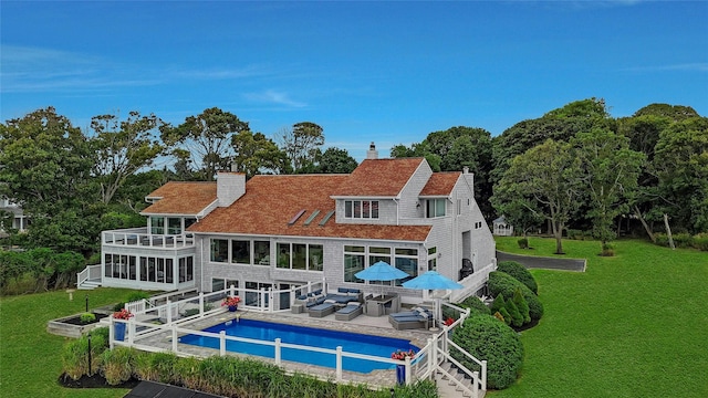 rear view of property featuring a balcony, a yard, a chimney, a sunroom, and an outdoor hangout area