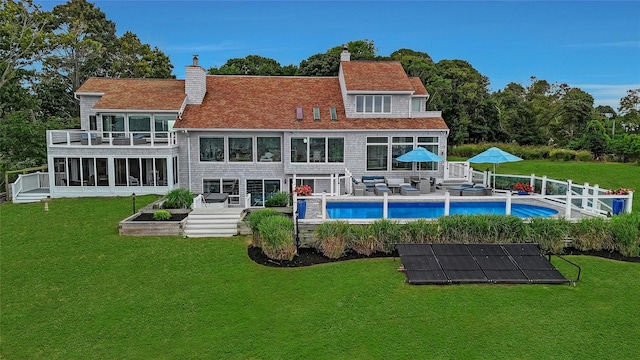 rear view of property with a chimney, an outdoor pool, outdoor lounge area, and a lawn
