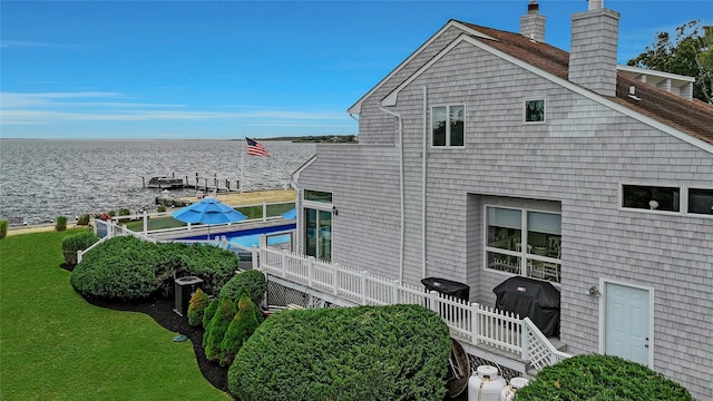 exterior space featuring cooling unit, a water view, and a chimney