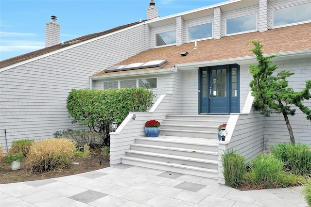 entrance to property with a chimney and roof with shingles