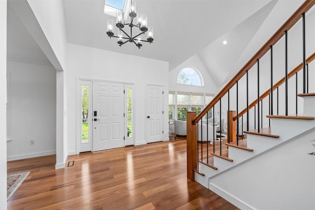 foyer featuring wood finished floors, high vaulted ceiling, stairway, baseboards, and a chandelier