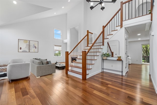 living room featuring stairway, an inviting chandelier, wood-type flooring, and high vaulted ceiling