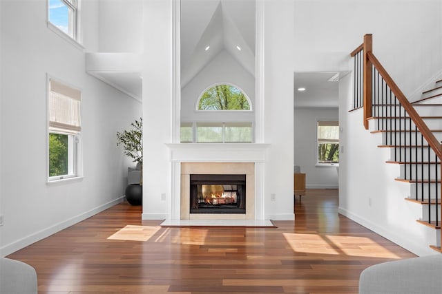 unfurnished living room with a fireplace with flush hearth, stairs, a wealth of natural light, and high vaulted ceiling