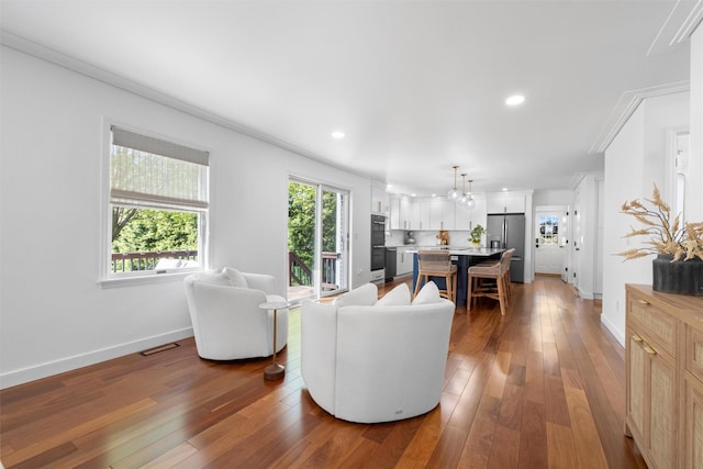 living room featuring baseboards, crown molding, wood-type flooring, and visible vents