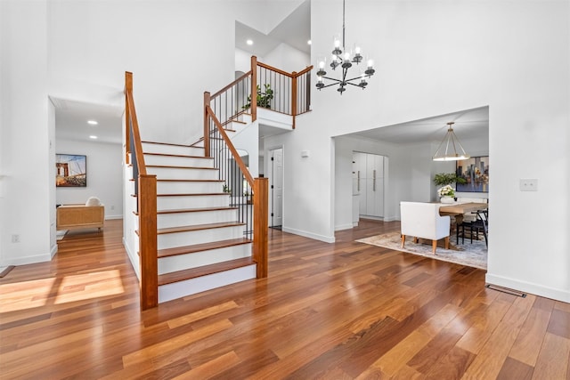 stairway featuring wood finished floors, recessed lighting, a notable chandelier, a high ceiling, and baseboards